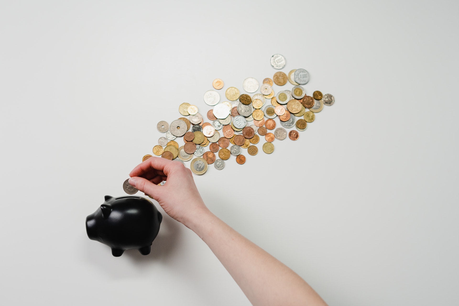 person inserting coin into black piggy bank with coins scattered around