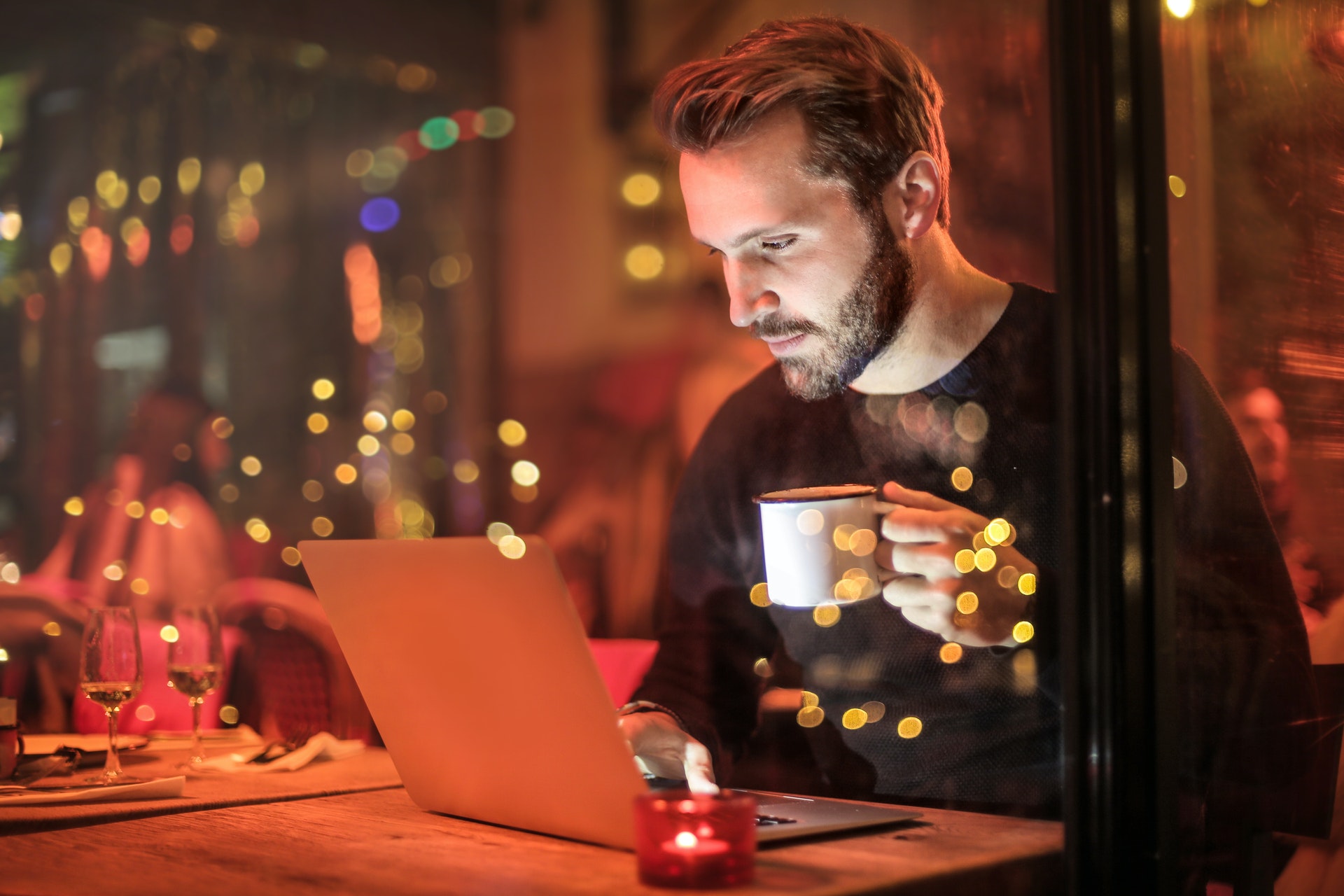 man working on laptop with coffee in hand at cafe