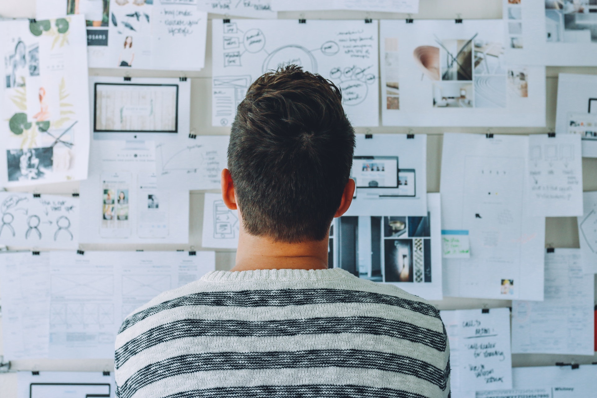 man looking at wall covered with graphs, plans and notes