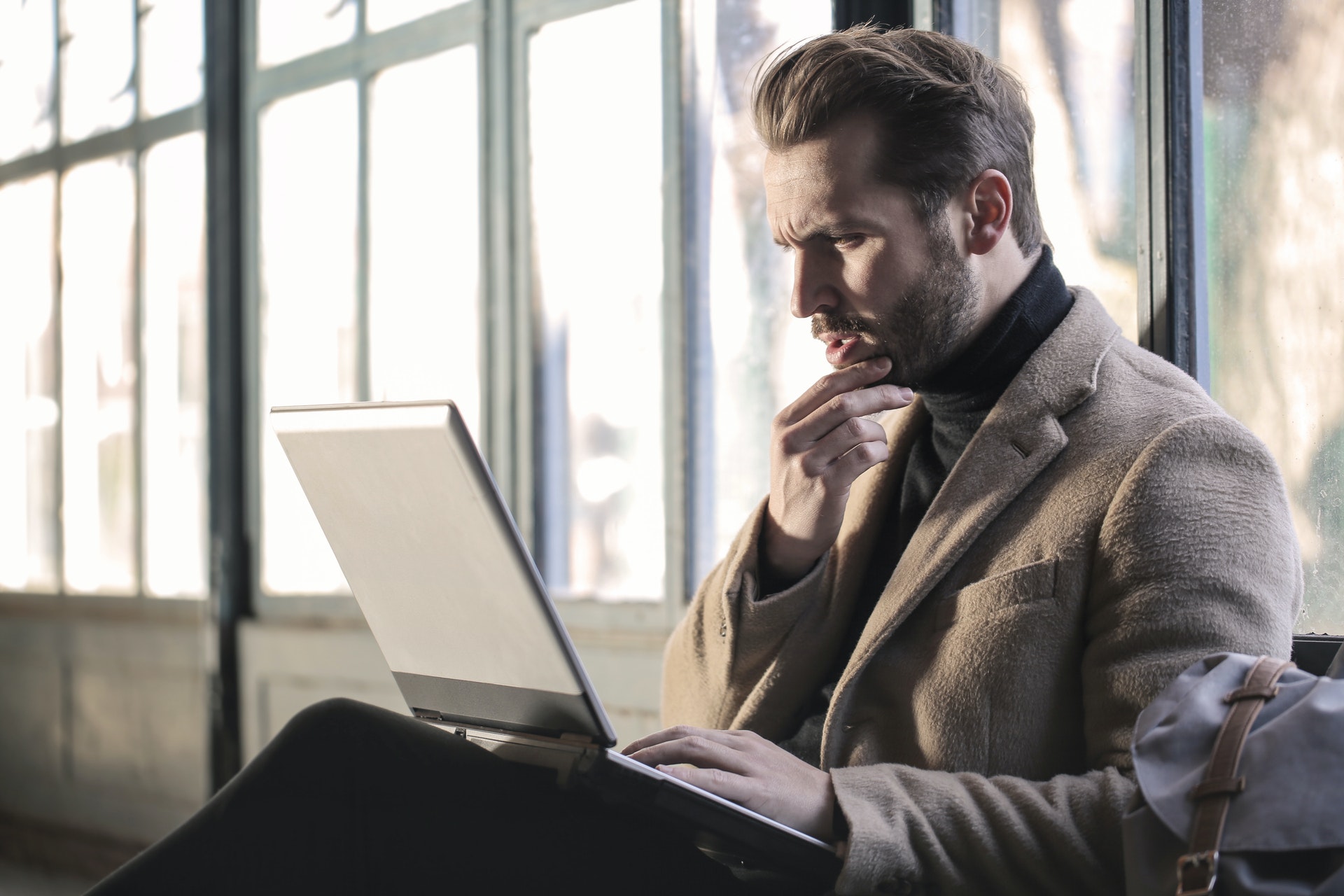 Man wearing turtleneck looking at laptop thinking