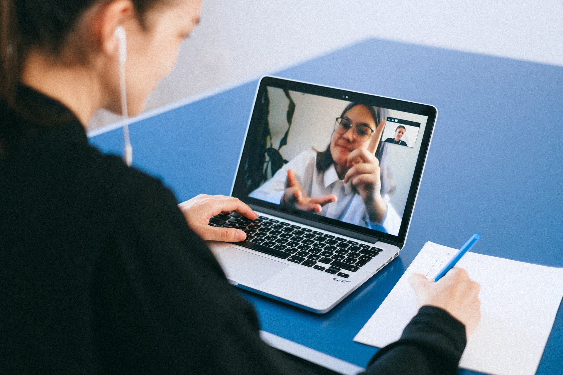 Two people on a call on laptop while one writes on paper