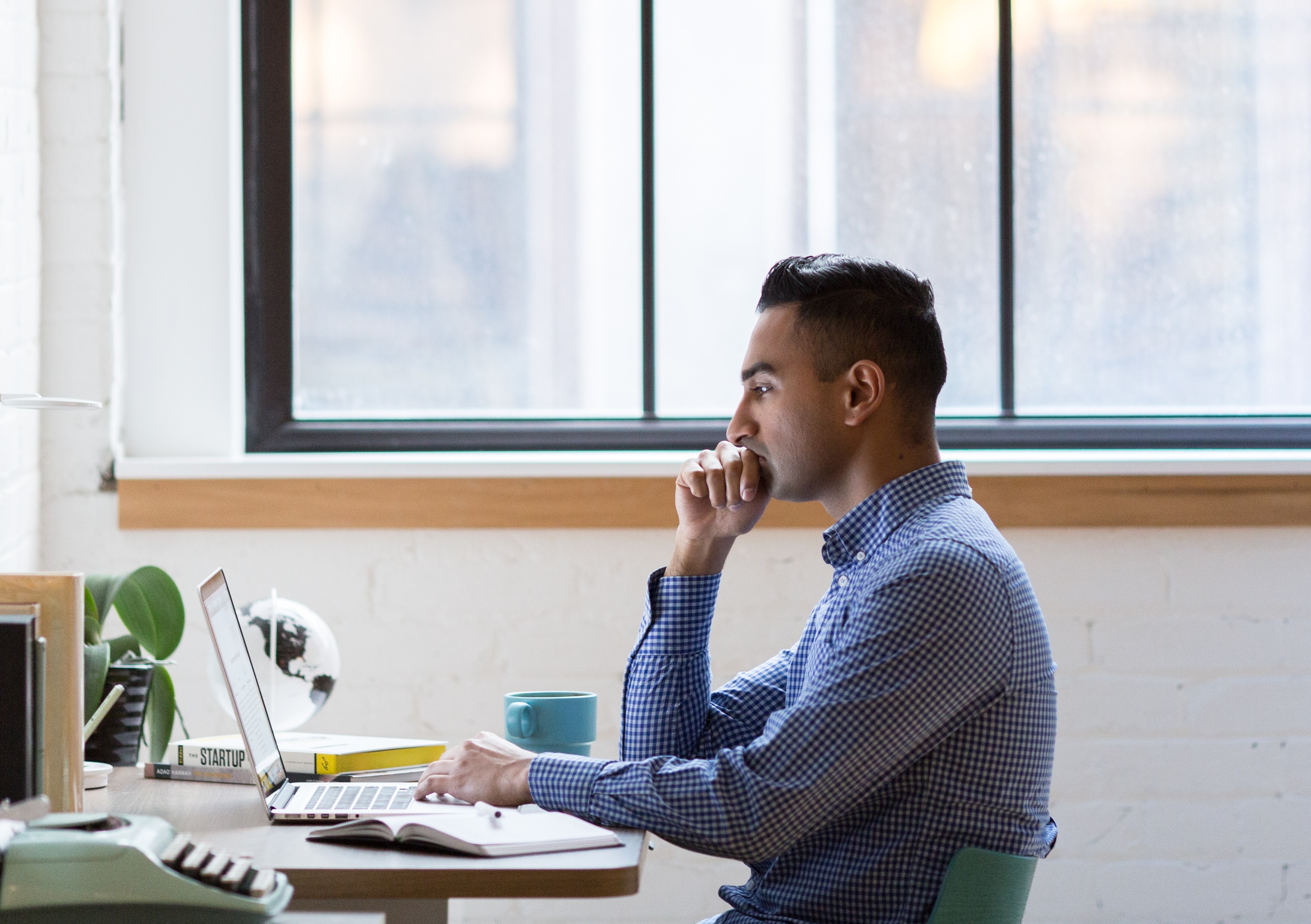 man in blue shirt looking at laptop thinking