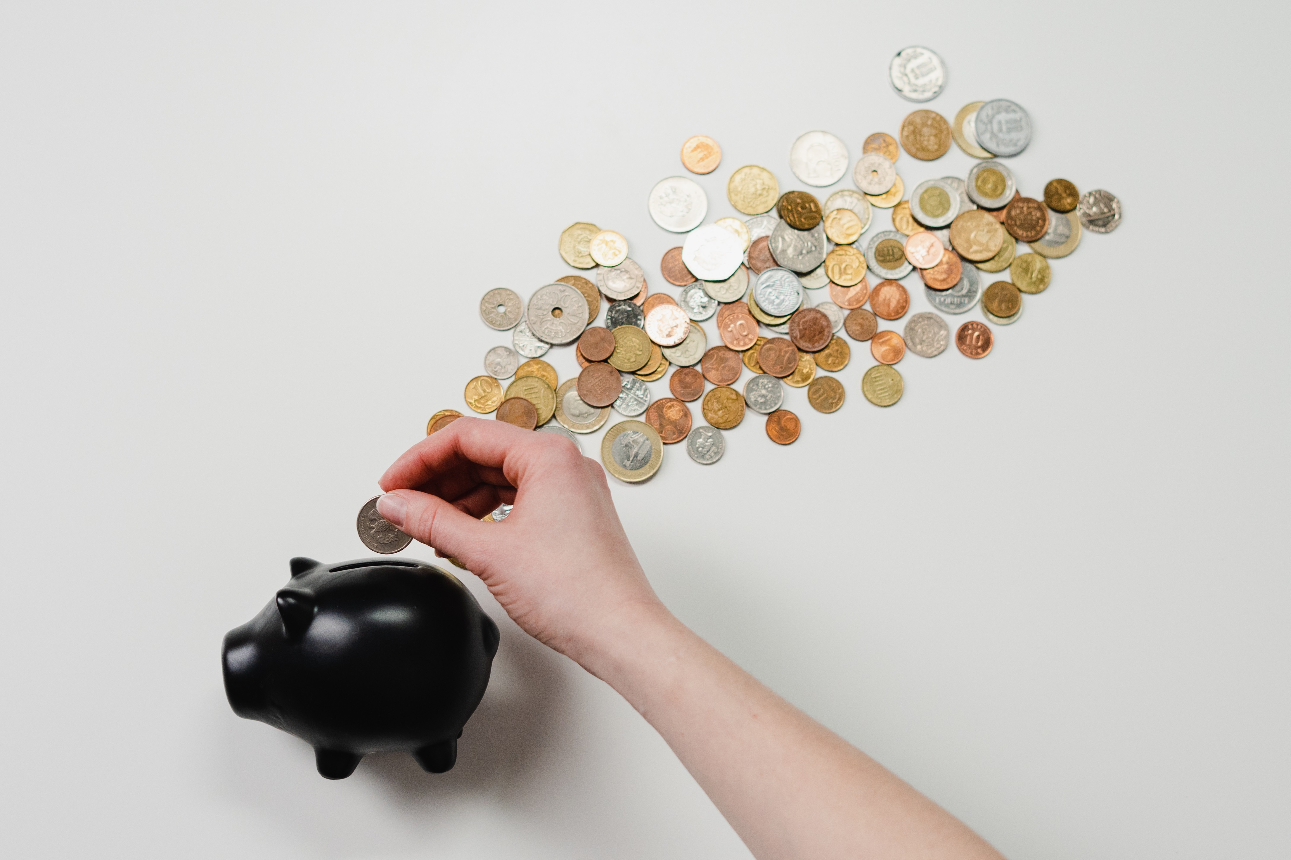 hand putting coins in piggy bank with coins all around