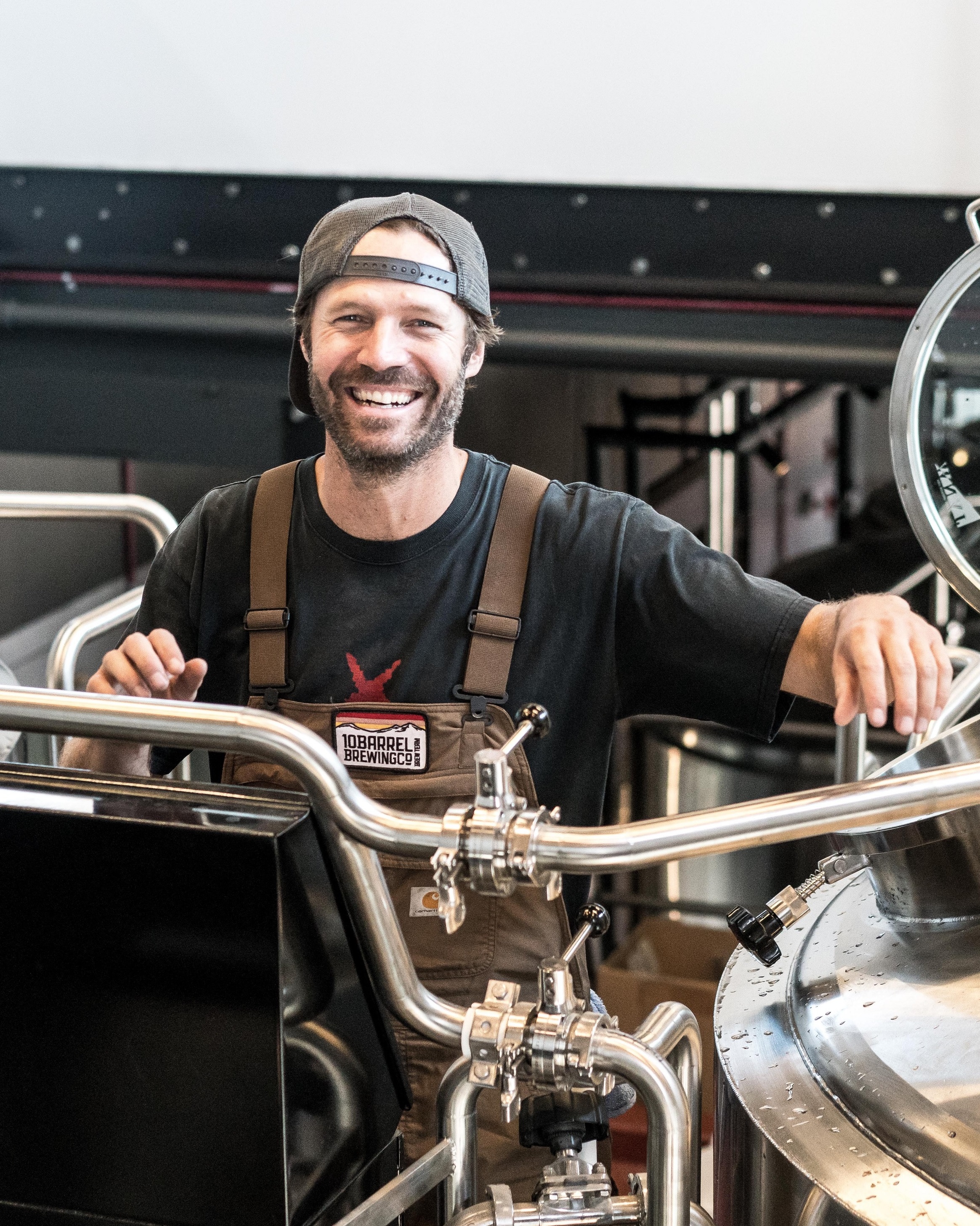 beer brewer standing next to vats smiling