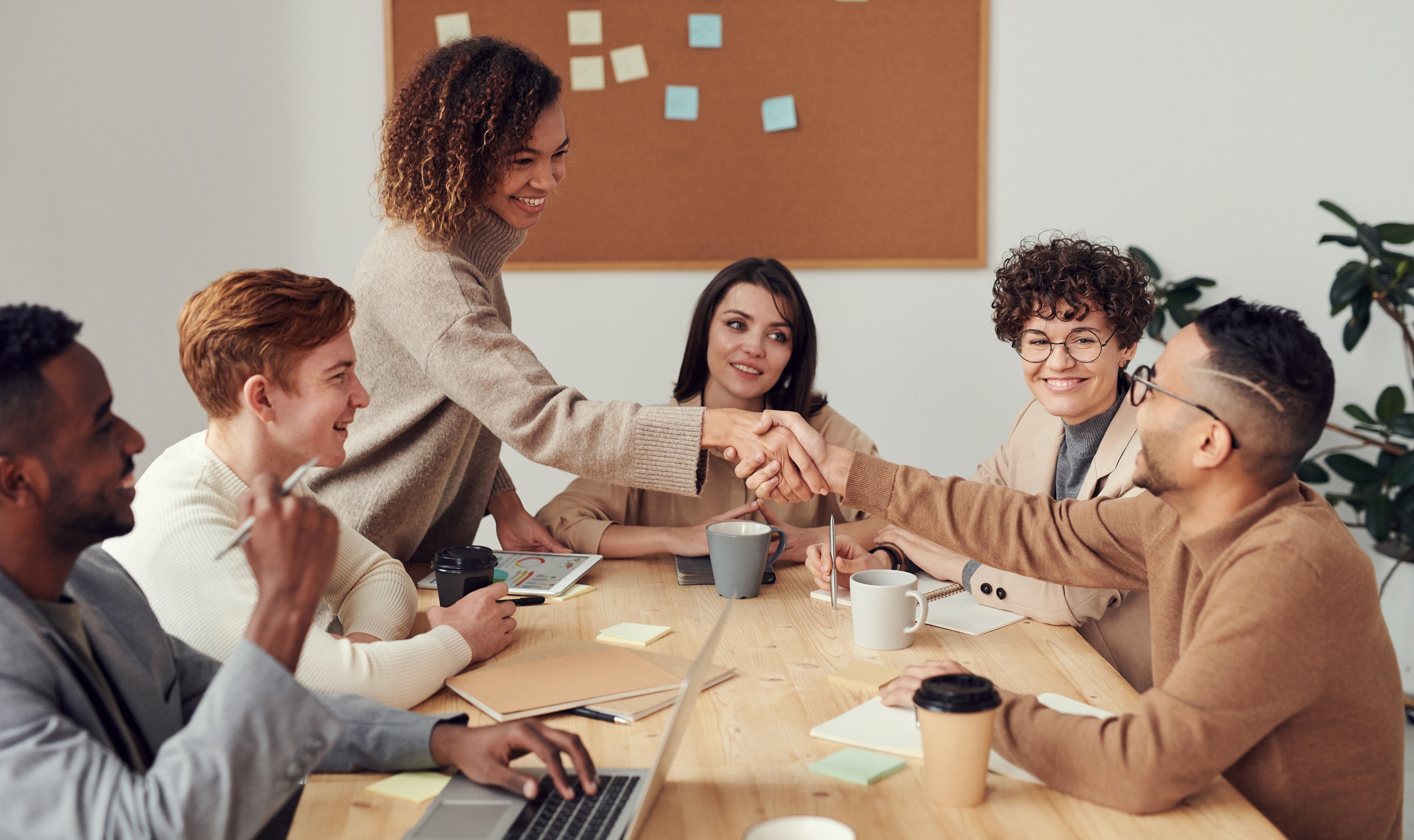 two people shaking hands over table with work colleagues