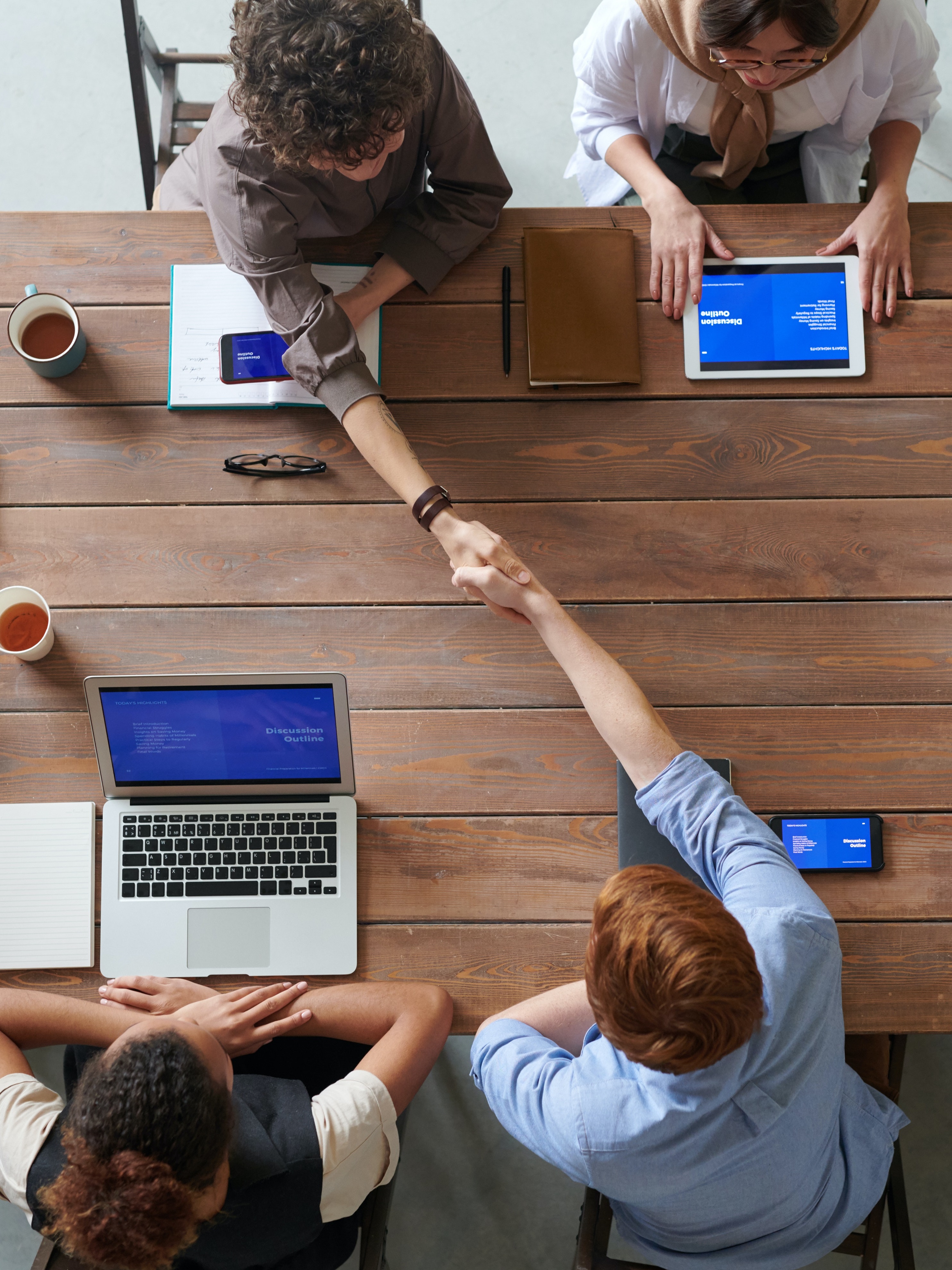 two people shaking hands over wooden table with colleagues