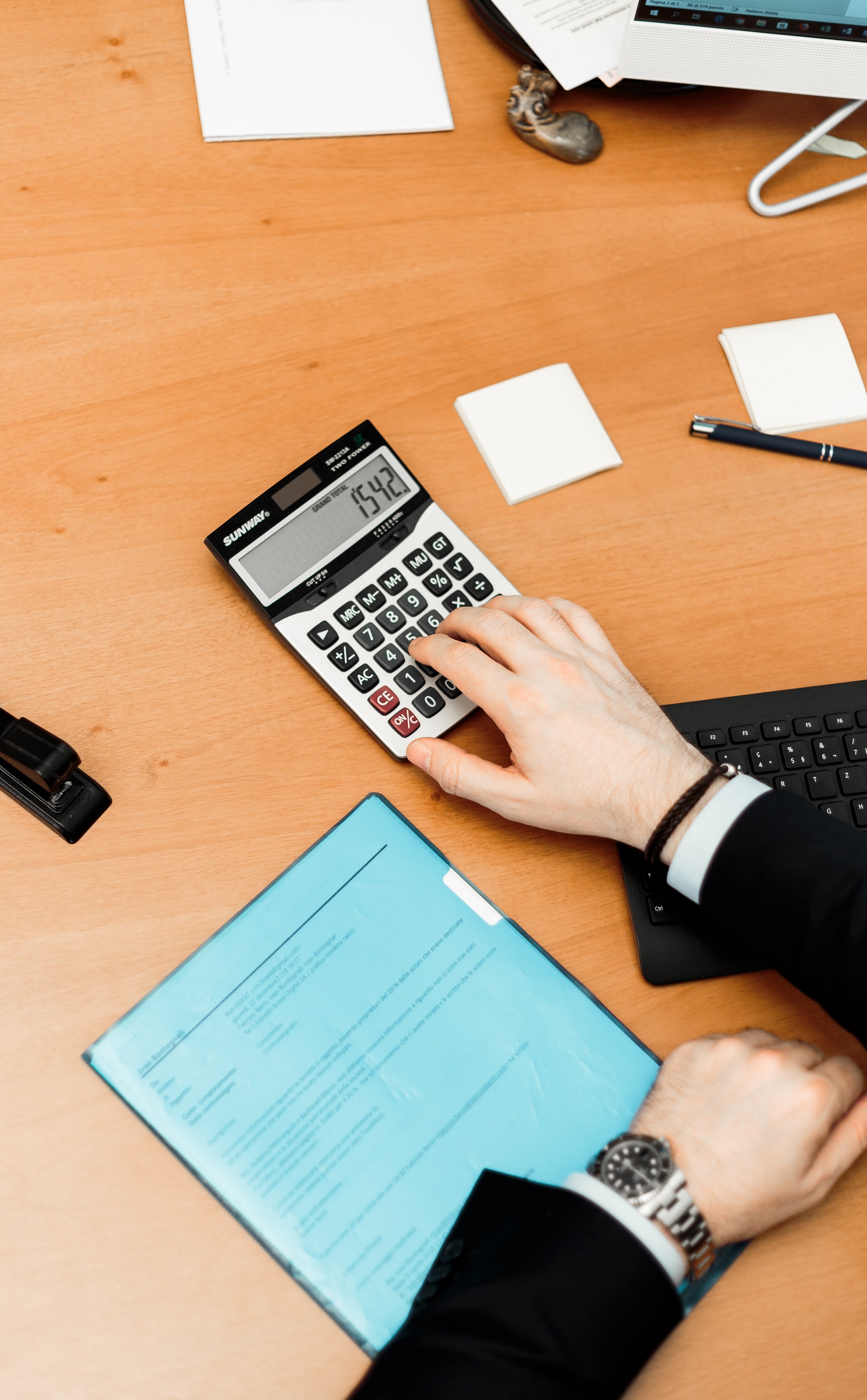 man with watch using calculator next to files