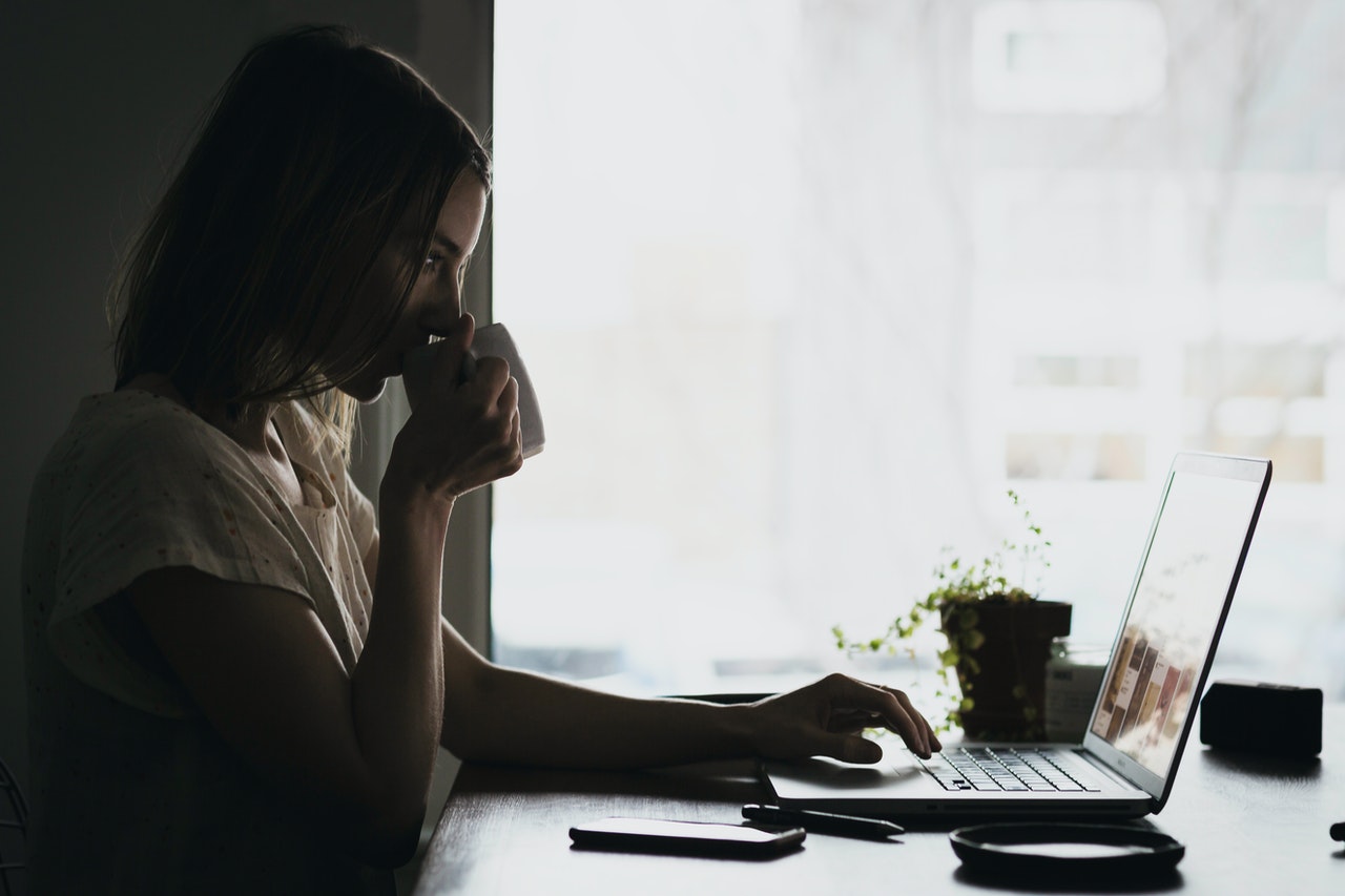 woman drinking cup of coffee while working on laptop