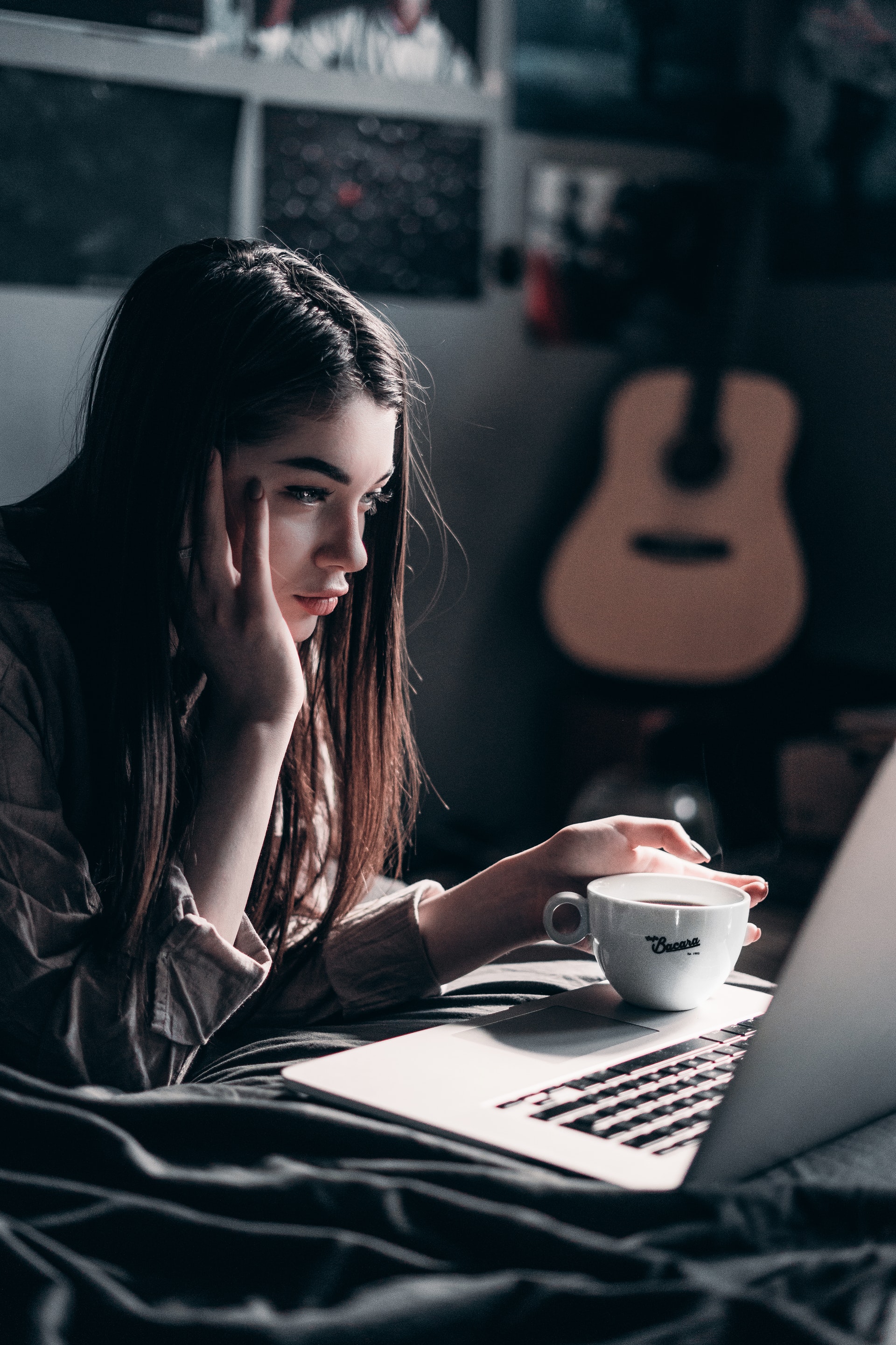 woman holding cup of coffee while looking at laptop