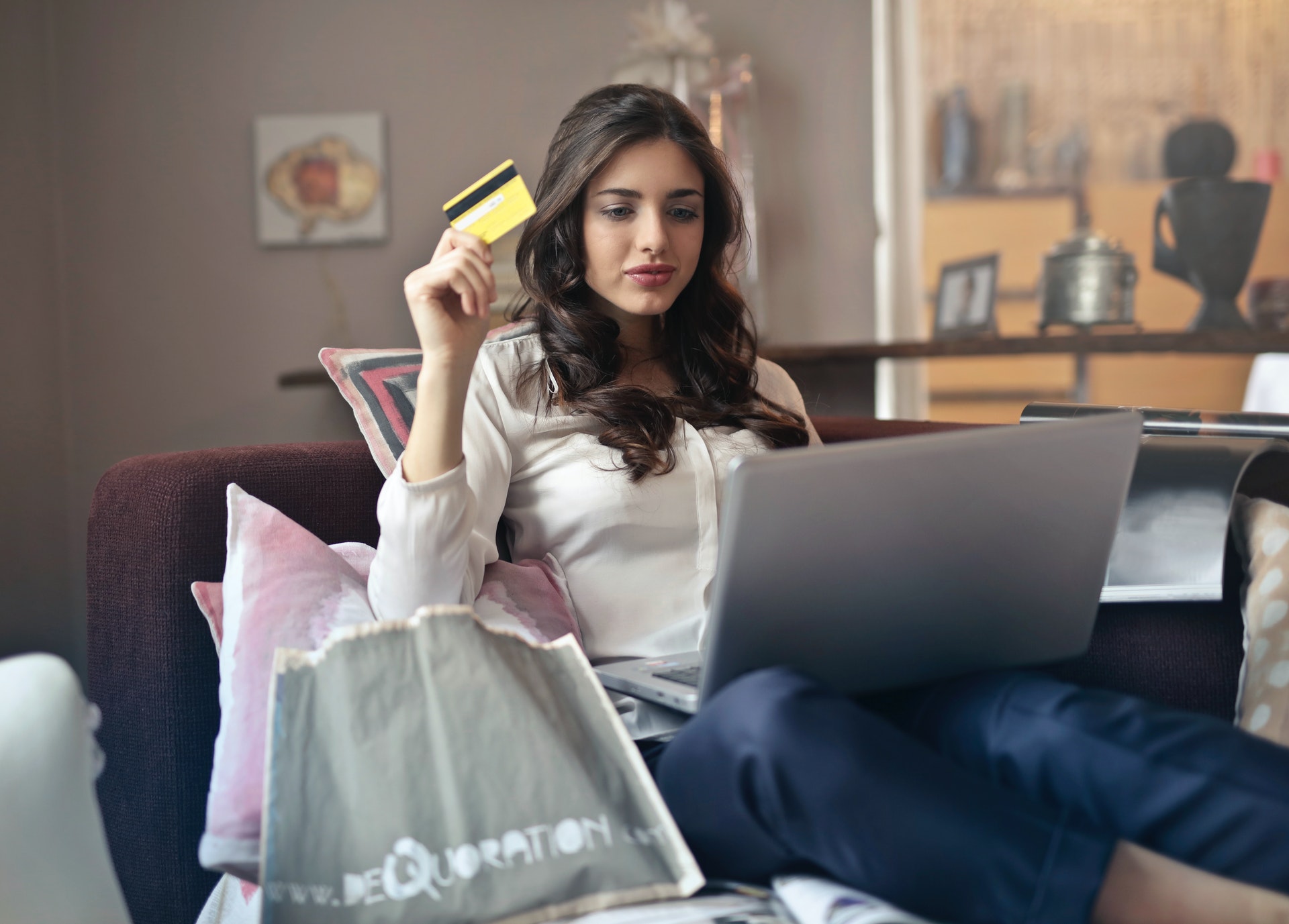 woman with laptop on sofa holding credit card